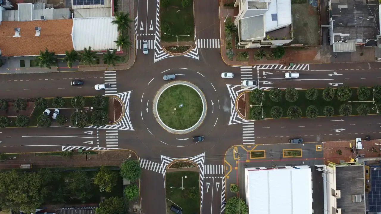 Vista aérea de rotatória urbana com faixas e marcações viárias brancas e amarelas