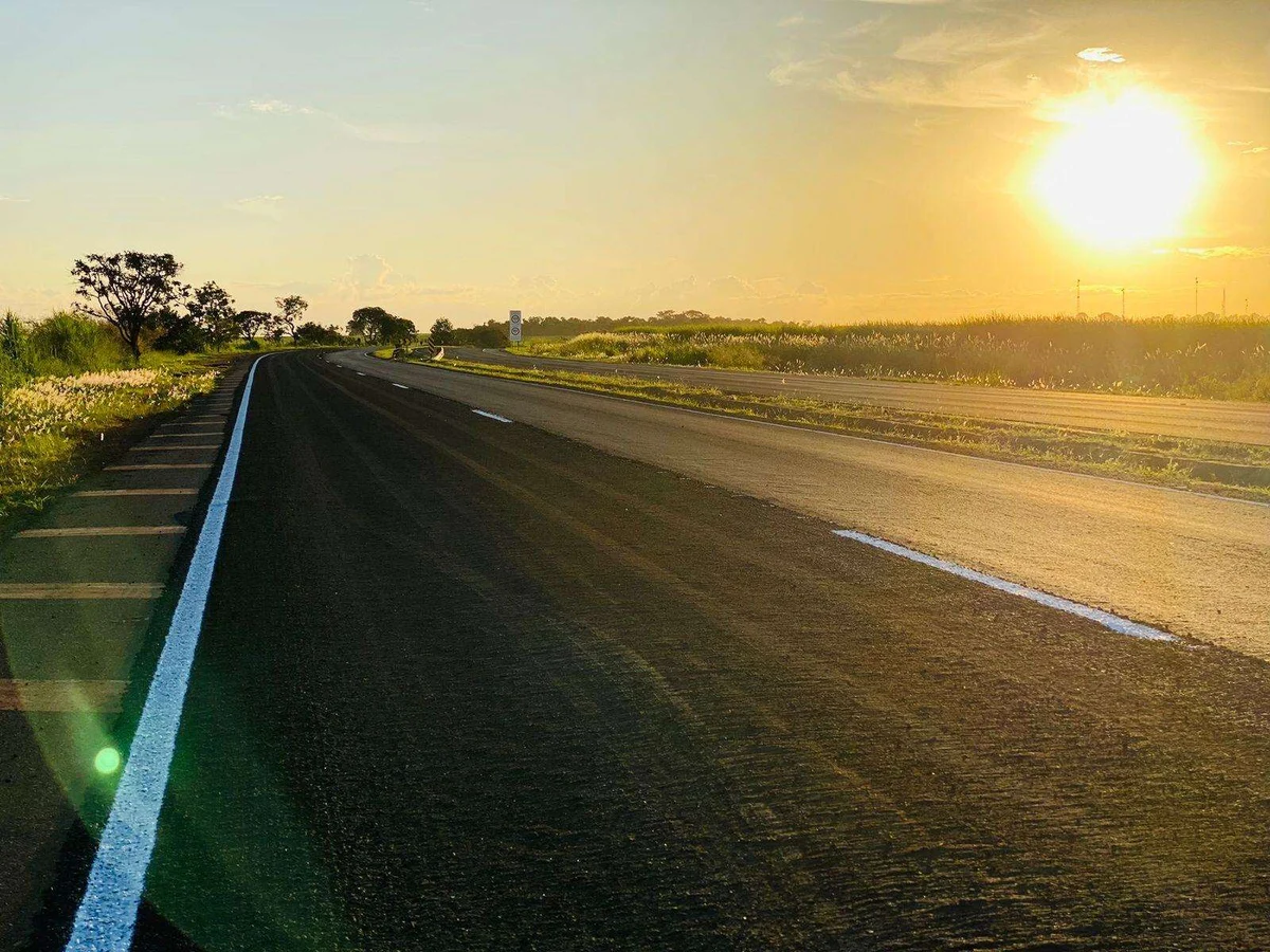 Sinalização horizontal branca em trecho rodoviário ao pôr do sol